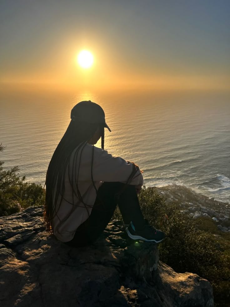 black woman sitting near the ocean at sunset
